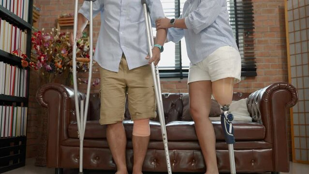 woman wearing prosthetic legs helps her husband injured in an accident using crutches.equality concept, disability, life difficulties
