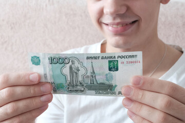 A European young man holds Russian paper banknotes in his hands, rubles in denominations of 1000 . Concept - earned money, student budget, scholarship holder. - obrazy, fototapety, plakaty