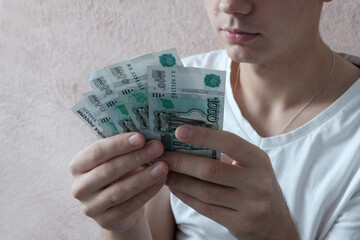 A European young man holds Russian paper banknotes in his hands, rubles in denominations of 1000,  Concept - earned money, student budget, scholarship holder. - obrazy, fototapety, plakaty