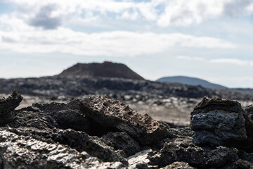 Fototapeta na wymiar Select focus close up of pieces of lava rock in lava field near mountain Fagradalsfjall with in background out of focus fissure vent of 2021 in Geldingadalir volcano, Iceland