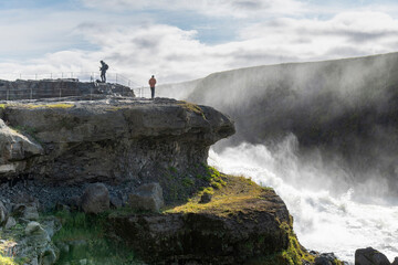 Some of the steps or staircases of the Gullfoss waterfall located in the canyon of the Hvítá river in southwest Iceland with bright sun in sky and tourists on viewpoint above