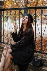 A girl in retro coat smoking cigarette sitting on fence in the autumn park