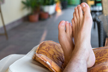 Male feet in the foreground crossed and resting on cushions on the terrace. Relaxing day and view...