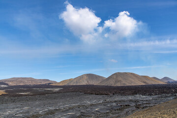 Fototapeta na wymiar Panoramic view over large black lava field with mountains in volcanic landscape on Reykjanes Peninsula, Iceland, near mountain Fagradalsfjall volcano area against a white clouded blue sky