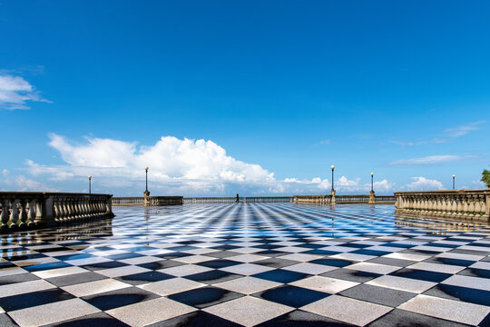 Low angle view over Terrazza Mascagni scenic seaside promenade in Livorno, Italy, with elegant balustrade and wet black-and-white checkerboard pavement with one person in distance 