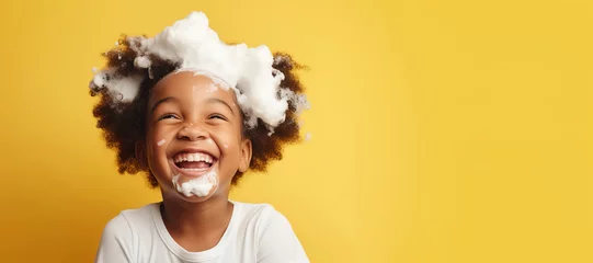 Fotobehang banner copyspace Little smiling african American child boy with big soap foam on head in hair on solid yellow background, Kids hygiene, Shampoo, hair treatment and soap for children, Kids bathing time © Jim1786