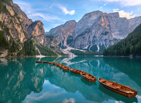 A calm morning by the clear lake Lago di Braies in the Italian Dolomites. The reflection of the mountains on the surface and the foreground with a row of wooden boats creates a great atmosphere.  A we