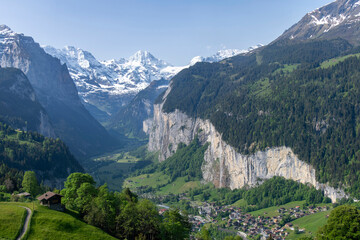 Panoramic view over Lauterbrunnen, Switzerland with high cliffs and Staubbach Waterfall and snowcapped mountains of Bernese Alps in background
