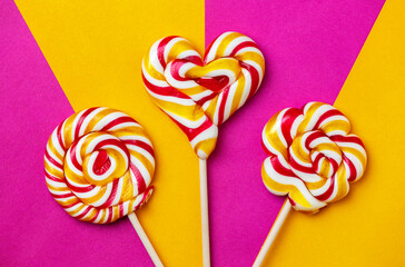 Three large lollipops on a stick in the shape of a circle, a flower and a heart on a bright orange-purple background, handmade