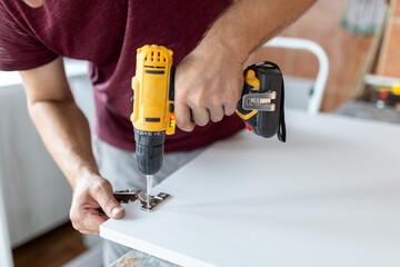 Man holding cordless screwdriver machine and screws lie for screwing a screw assembling furniture at home - obrazy, fototapety, plakaty