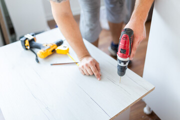 Close up worker hands holding cordless drill for kitchen assembly furniture indoors.