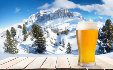 glass of beer on wooden table against winter landscape