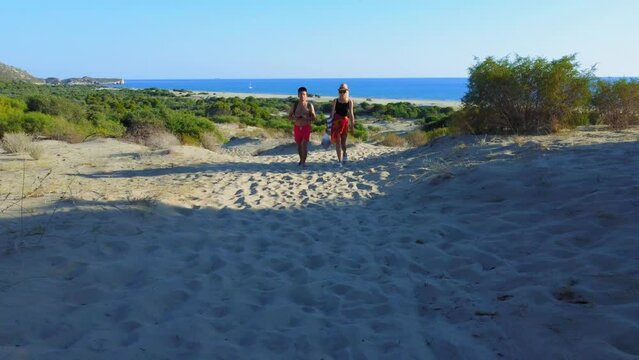 Drone flight of couple of happy travelers walking along sand dunes on beautiful beach of Patara on Mediterranean coast. Wanderlust, travel, and social media content. Turkey. Mountains and seas. Heat.