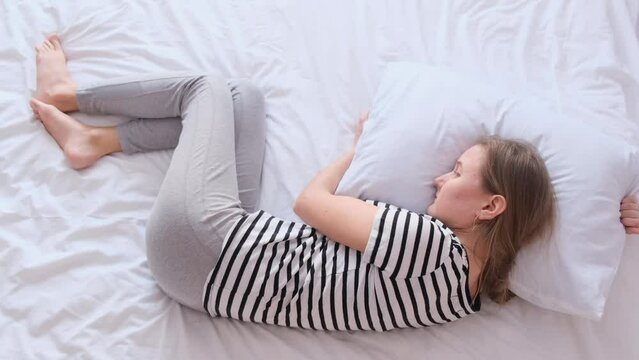 Top view of lonely young woman curled up in fetal position while lying in bed.