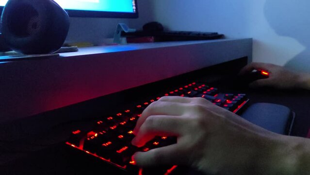 Close up hand playing game using the keyboard keys W A S D on the dark. Gamer playing shooting game on computer with mechanic keyboard with red backlight. Online esport streaming game online