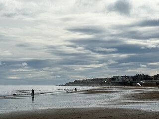 Dark dramatic rain clouds above surf at the beach with golden sand and waves in Whitley bay, Newcastle, England. Typical English weather with rain. People walking the dog at the beach.