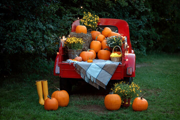 A vintage red classic old truck filled season flowers hay and festive fall orange pumpkins.