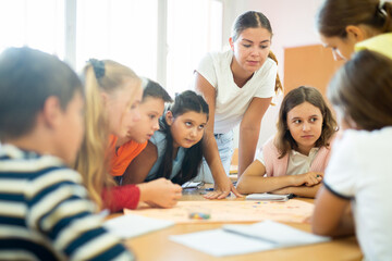 Fototapeta premium Teacher and group of kids playing board game in school after lessons. Children having fun playing interesting game.