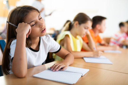 Tired young girl sleeping on desk in classroom during lesson. - Powered by Adobe
