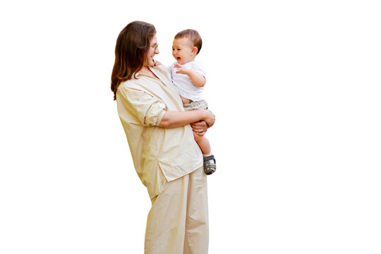 Mother Holds A Happy Toddler Boy Boy In Her Arms, Isolated On A White Background. Mom With A Smiling Baby In White Clothes, One Year Old Kid