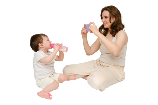 Woman mother takes a picture of a baby with a phone on a studio, isolated on white background. Mom blogger shoots a video from a child for a blog. Kid about two years old (one year nine months)
