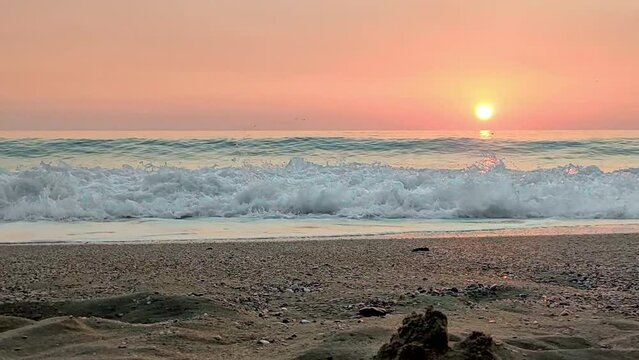 High sea wave rolls onto shore turning into white foam on background of pink sunset