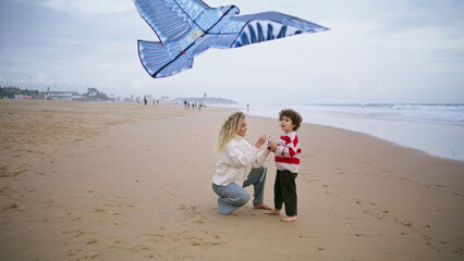 Mom playing kite kid at windy seashore. Caring parent helping son launching toy.