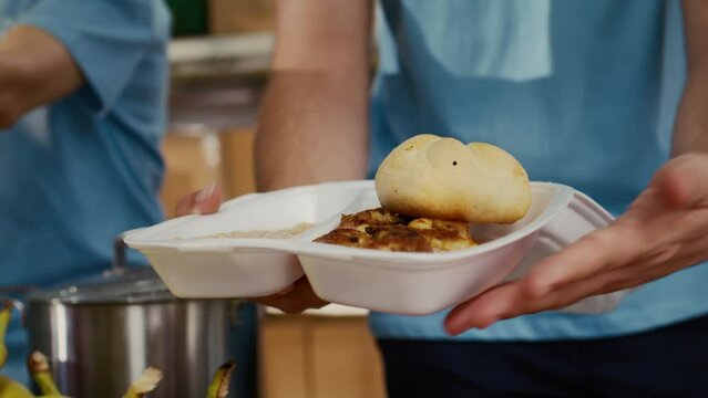 Close-up on caucasian man serving bread chicken and baked beans to poor hungry person at food drive. Detailed view of meal box from hunger relief team given to the needy. Selective-focus handheld.