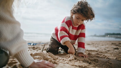 Cute boy building sand figures at ocean shore. Focused curly child rest outdoors