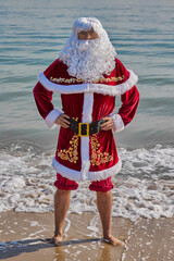 Santa Claus at sea on a hot summer day. Standing ankle-deep in water with his pants rolled up. Xmas or New Year's vacation in hot countries. Santa's summer vacation.