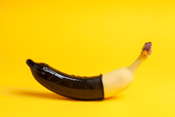 condom dressed on a banana on a yellow background, erection concept, safe sex concept, sexual male health concept - obrazy, fototapety, plakaty