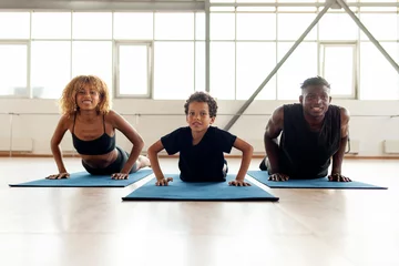 Fotobehang African-American family in sportswear doing exercises on yoga mat, young parents doing sports with their son © Богдан Маліцький