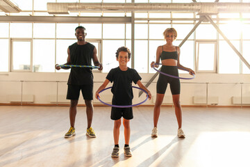 sporty african american family in sports uniform twists hula hoop and does exercises in the gym © Богдан Маліцький