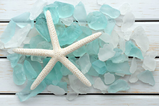 White starfish laying on turquoise sea glass collection - beach ocean shore background