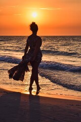 Woman on the seashore in a beautiful evening scenery. Girl walking on the beach with the setting sun in the background. Photo taken at the Baltic Sea in Leba, Poland. - 659687269