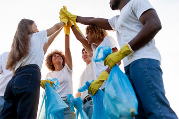 team of volunteers in gloves and with garbage bags rejoice together at success and high five - obrazy, fototapety, plakaty