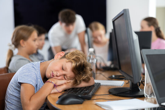 Boy student tired and lies down at computer desk during lesson in classroom