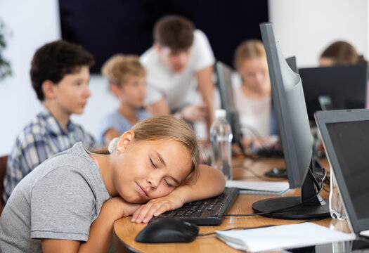 Sleepy underage girl sitting at computer table during IT courses for children