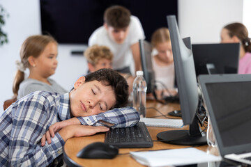 Boy student tired and lies down at computer desk during lesson in classroom