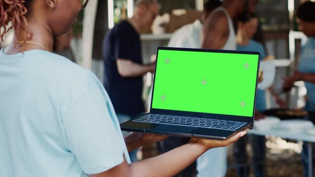 Detailed view of african american female volunteer holding laptop with isolated copyspace display for customization. Black lady holds minicomputer with green screen chromakey template in her hands.