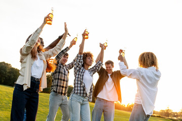 group of multiracial friends at party with bottles of beer dancing and having fun outdoors, group of people singing