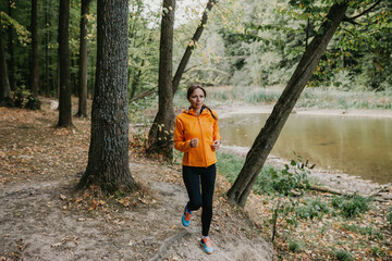 Fototapeta premium A photo of a beautiful young woman running in the park. Fresh air at forest. A healthy lifestyle