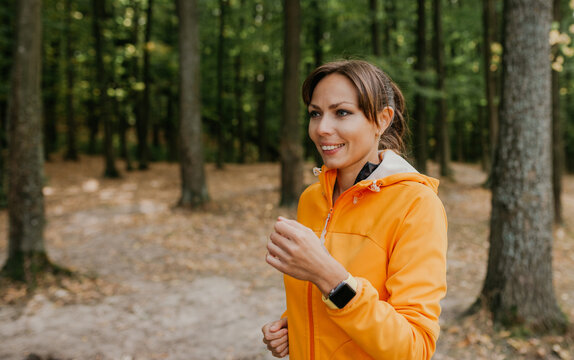 A photo of a beautiful young woman running in the park using smartwatch. Fresh air at forest. A healthy lifestyle