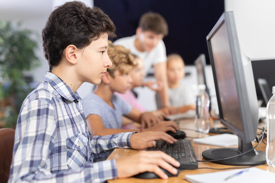 Minor male student sitting at computer together with other attendees of IT courses