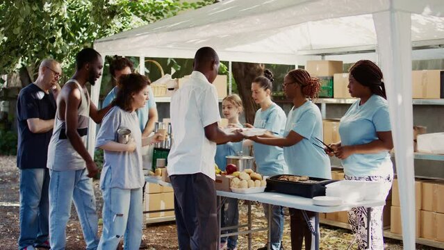People from many backgrounds assemble outside to distribute non-perishable donations and help the poor and homeless. Multiracial volunteers provide needy individuals with free, freshly prepared meals.