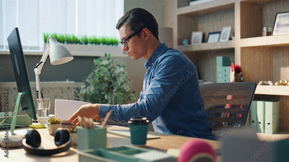 Wall mural busy startuper flipping notebook pages at computer table. serious man working