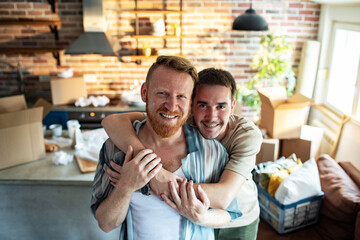 Portrait of a smiling young male gay couple hugging in their new apartment after moving in