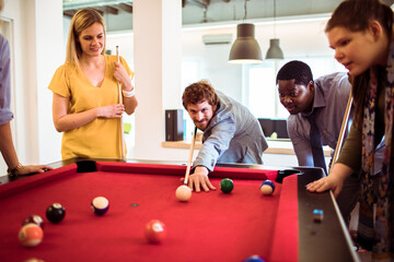 Young and diverse group of business friends playing pool in the modern office