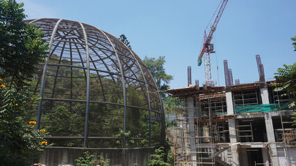 Large metal dome aviary for bird conservation next to a building construction site where crane...
