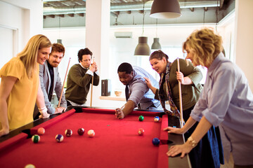Young and diverse group of business friends playing pool in the modern office